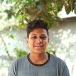 Smiling young man with short hair outdoors in Bangladesh, under a tree.